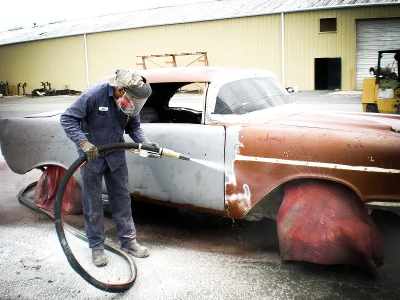 Operator removing a coating from a classic vehicle
